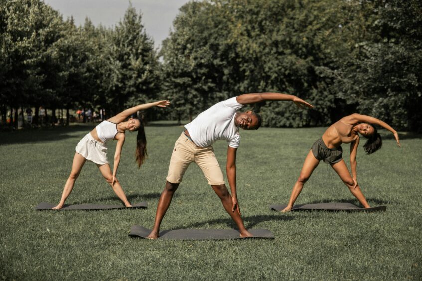 three people doing standing stretches on grass